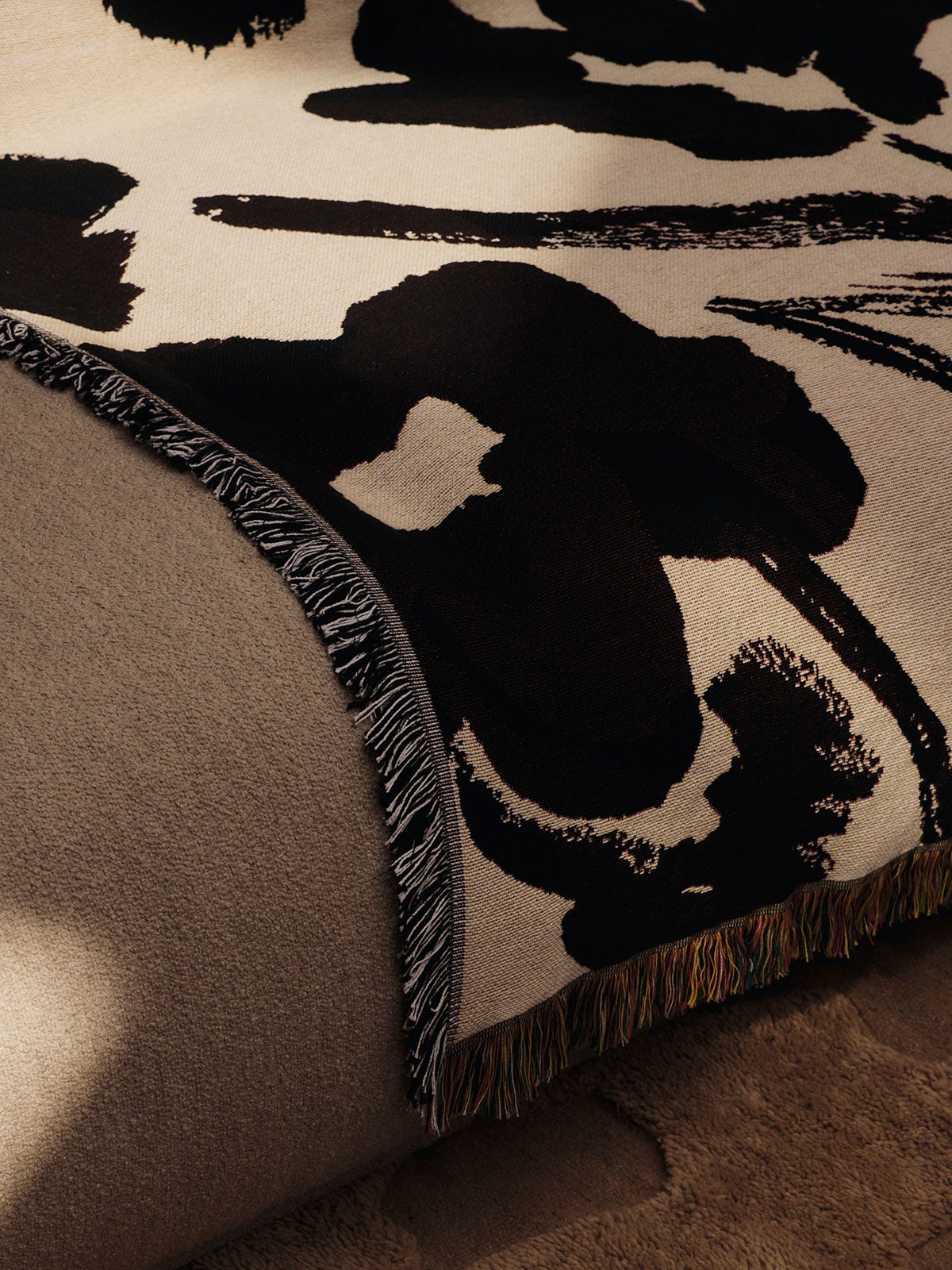 Cilla Tapestry Pläd i färgen Off-White/Dark Grape som ligger slängd över en soffkant